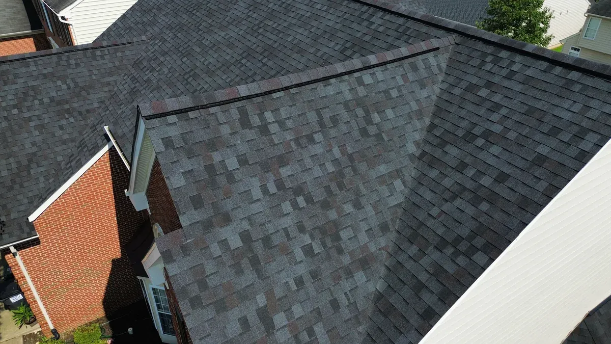 Close aerial detail of a finished dark multi-tone architectural shingle roof, showing two closed-cut valleys, a hip line, and new white drip edge along the eave