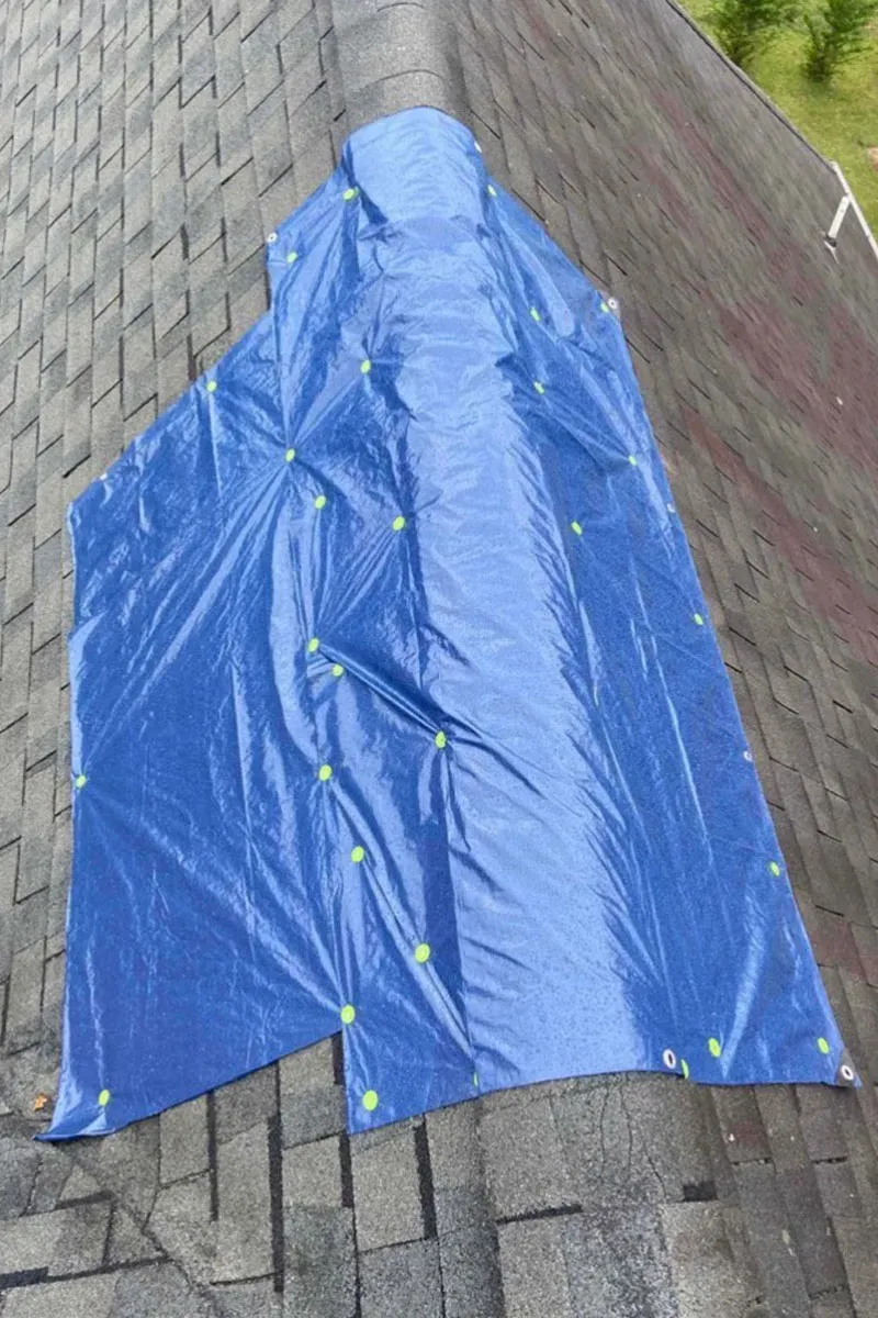 Blue tarp secured with cap nails in a grid pattern over a section of an asphalt shingle roof, running across the ridge