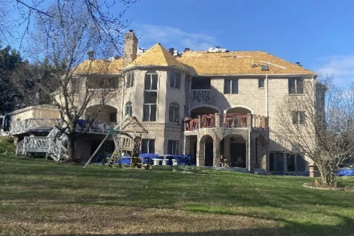 Full roof deck exposed across a large stone home, with tarps protecting the rear deck and patio furniture below