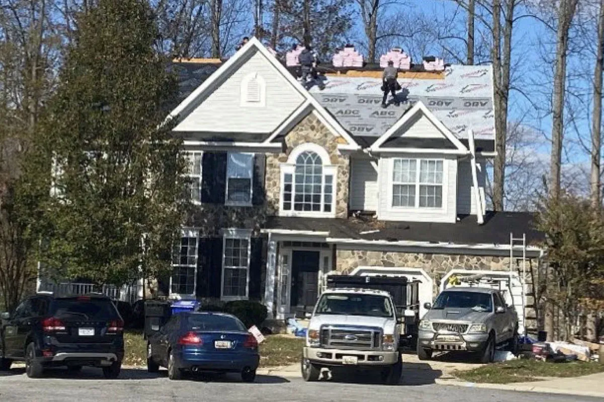 Synthetic underlayment installed over the roof deck of a stone-front colonial, with shingle bundles staged along the ridge and crew working the roof