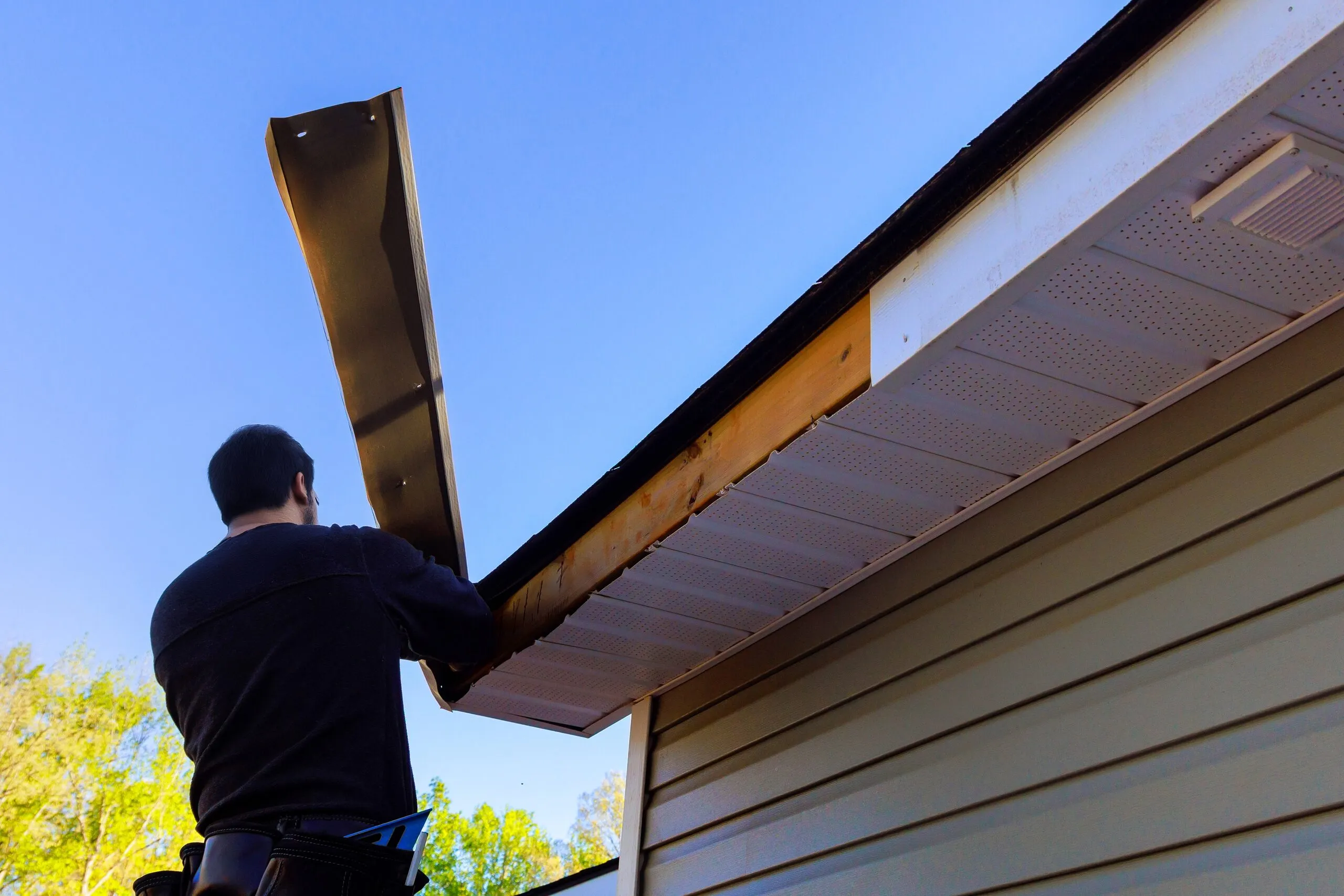 Installer lifting a length of fascia trim into place along the edge of a roof