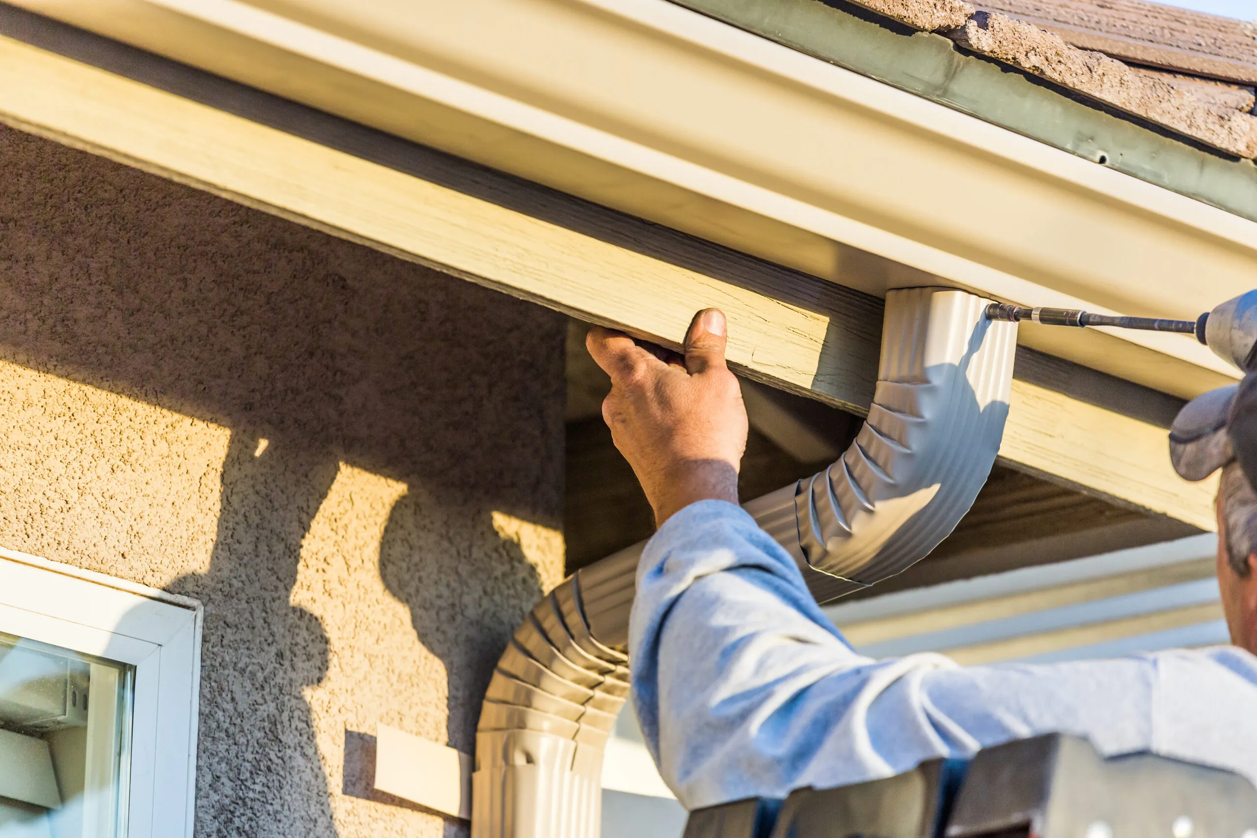 Installer fitting a downspout elbow to a gutter under the eave of a house