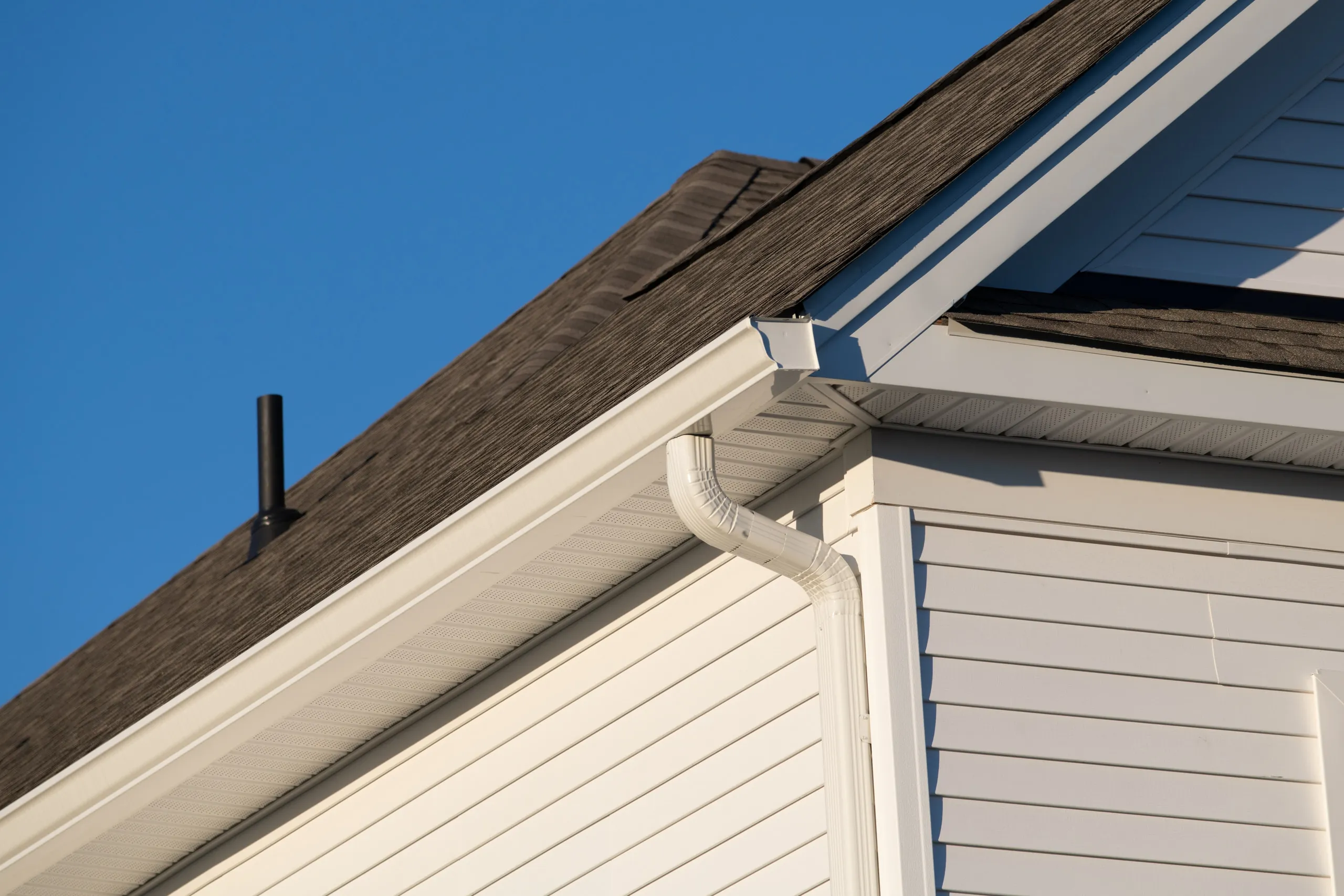 White K-style gutter and downspout running along a shingled roofline