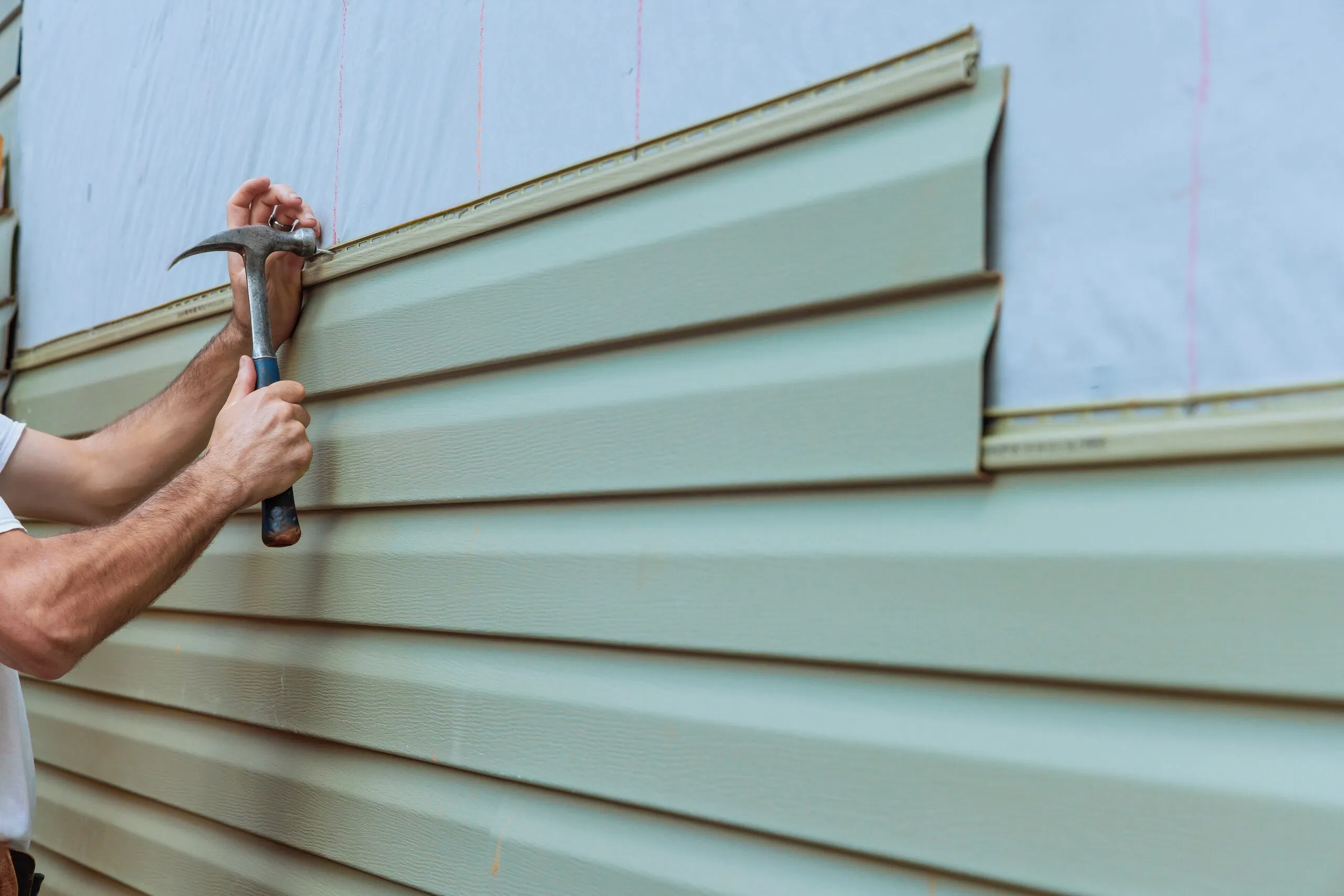 Installer nailing a course of horizontal vinyl lap siding onto a wall